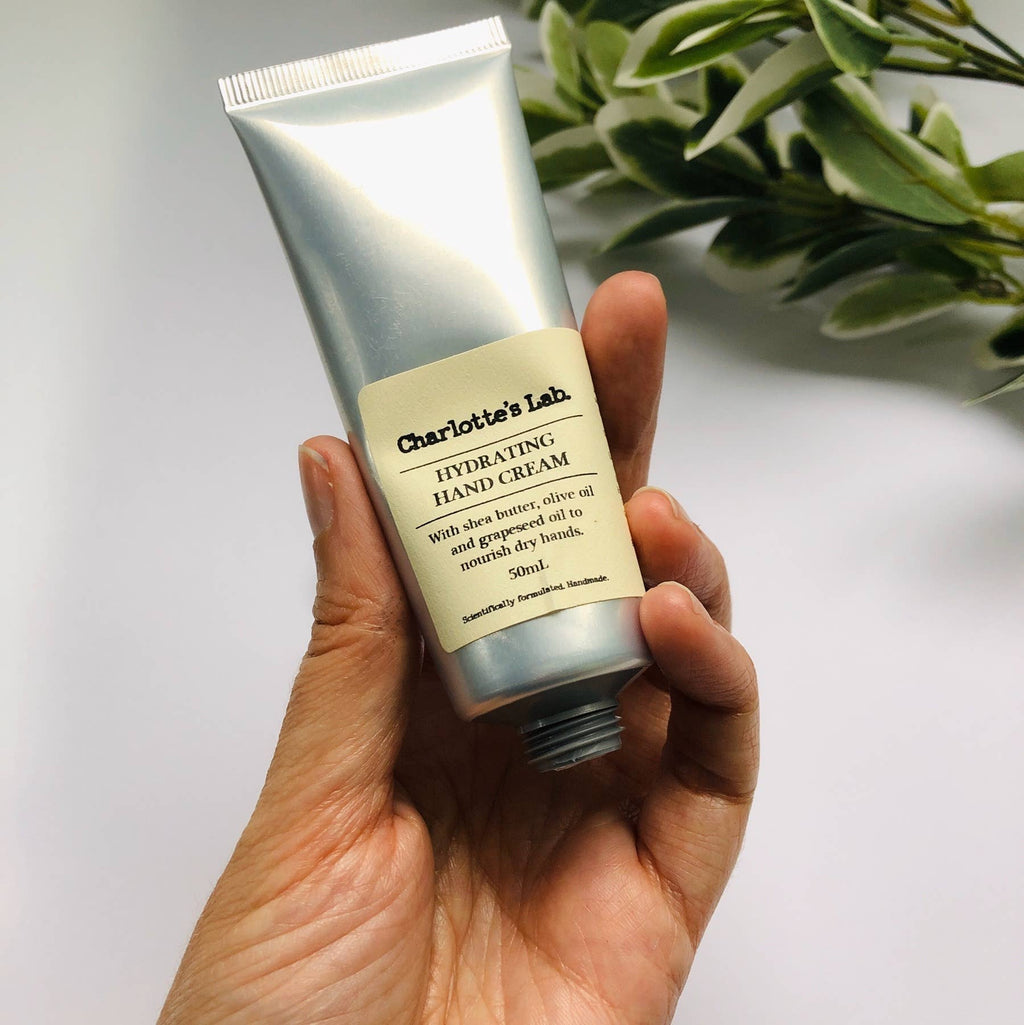 Hand holding a tube of Charlotte's Lab Hydrating Hand Cream with a light background
