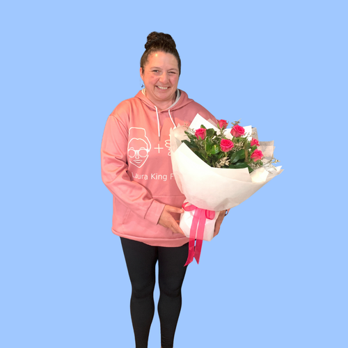 Laura holding Half dozen pink roses in a white wrapped bouquet in a 360 degree round style. Pink bow.