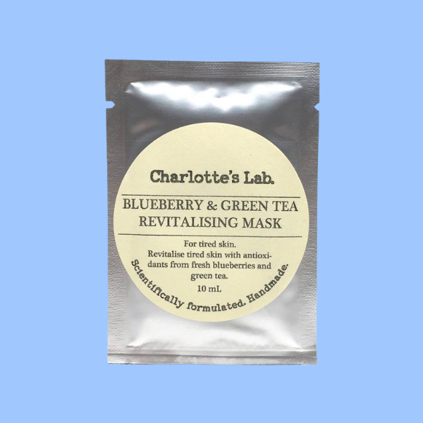 Charlotte's Lab Blueberry & Green Tea Revitalising Mask in a silver foil pouch with a cream-colored circular label, set against a solid light blue background.
