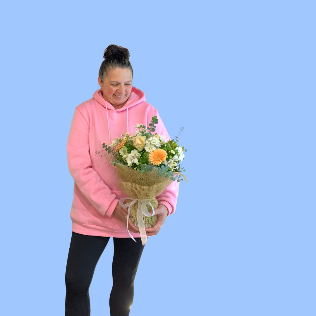 Laura King holding a bohemian looking bouquet of crisp pastel flowers in a vase wrapped in brown hessian with a white ribbon.