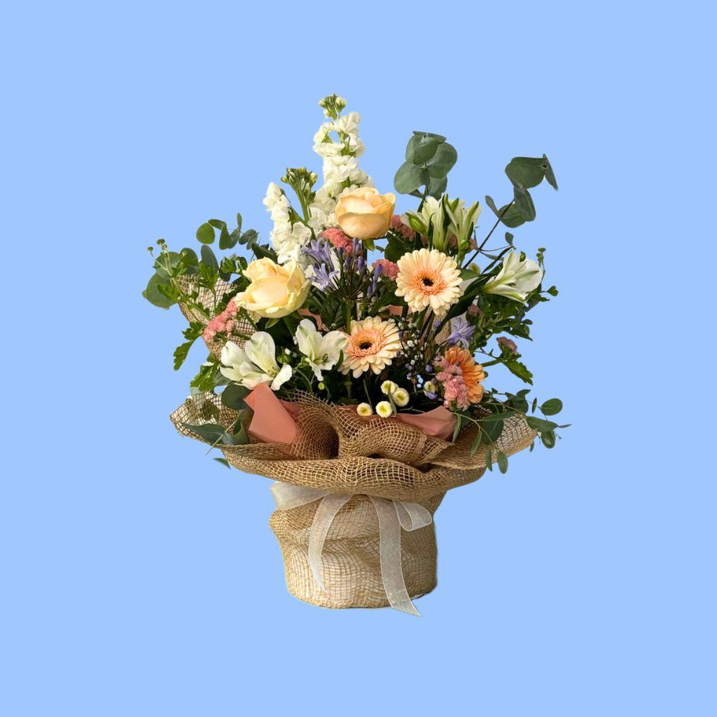 Pastels flower arrangement in a hat box wrapped in hessian and pink peal wrap with a white bow 
