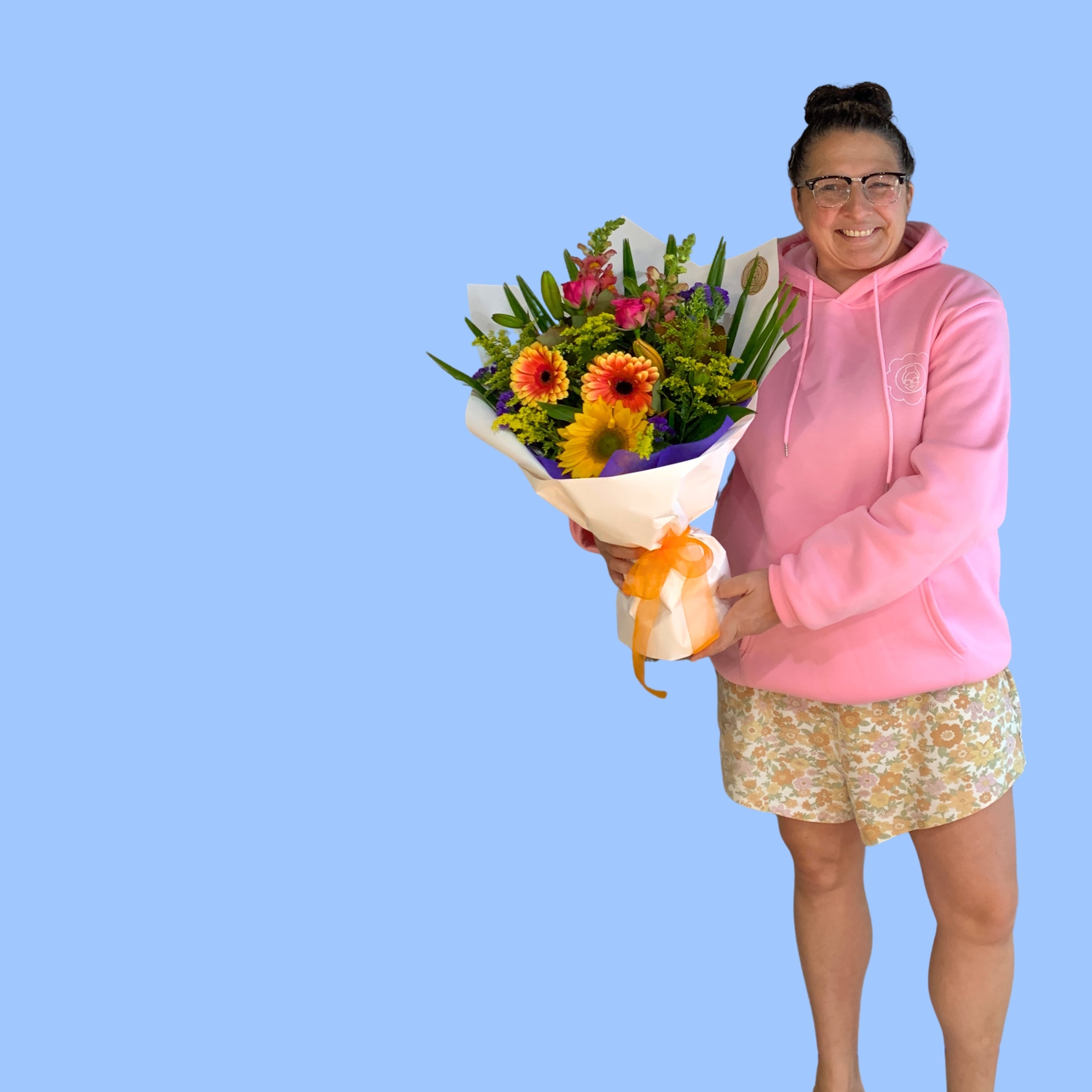 Laura King holding Mixed Bouquet of vibrant coloured flowers wrapped in craft and white with vibrant pink bow.