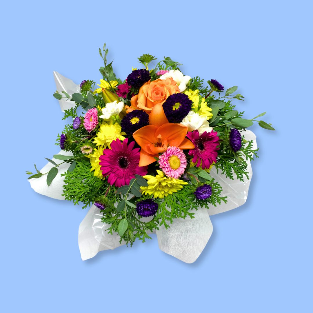 Top view of arrangement of mixed bright flowers against greenery and white tissue