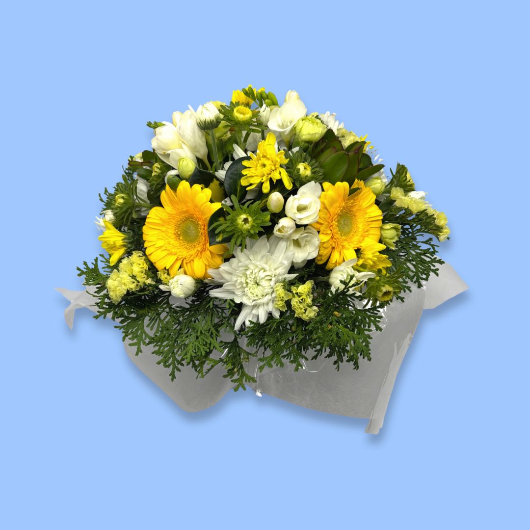 Box arrangement of crisp bold yellow and white flowers with greenery against white tissue.