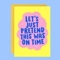 A yellow greeting card with a pink cloud graphic and blue text reading 'LET'S JUST PRETEND THIS WAS ON TIME', shown with a yellow envelope against a light blue background.