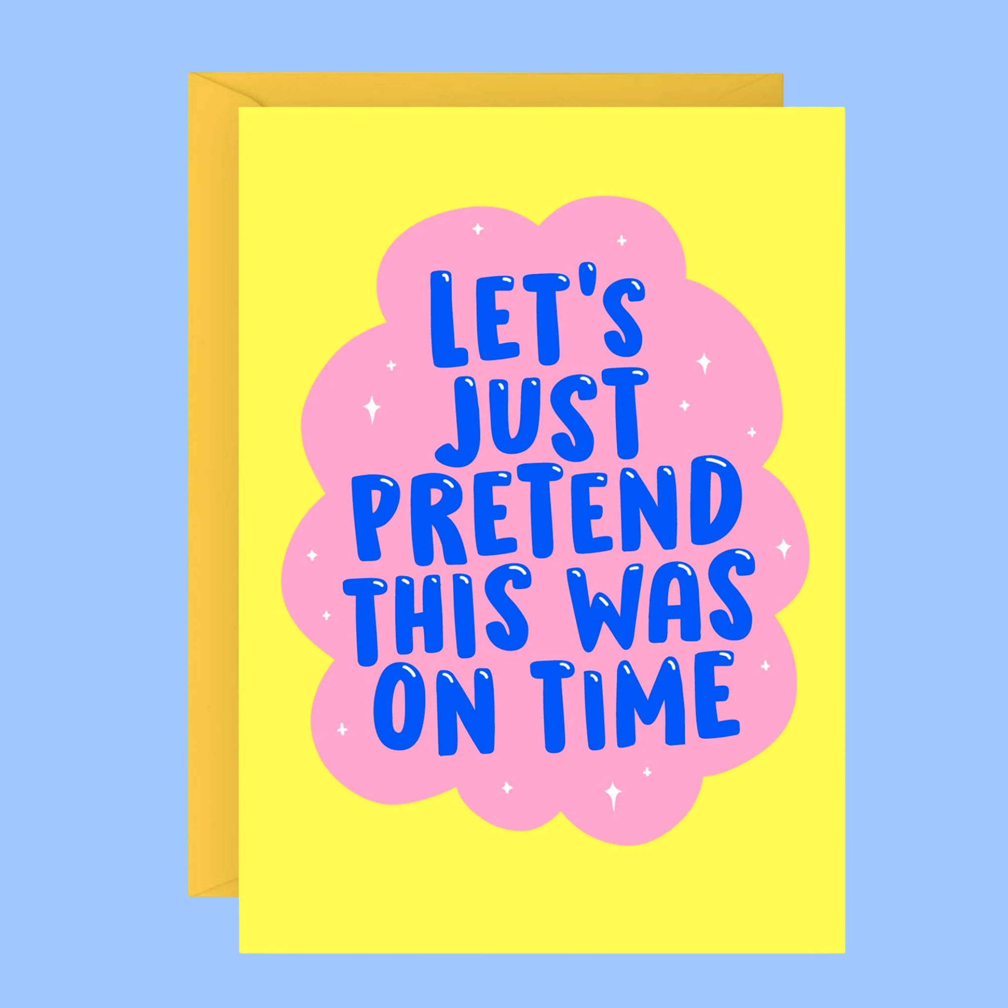 A yellow greeting card with a pink cloud graphic and blue text reading 'LET'S JUST PRETEND THIS WAS ON TIME', shown with a yellow envelope against a light blue background.