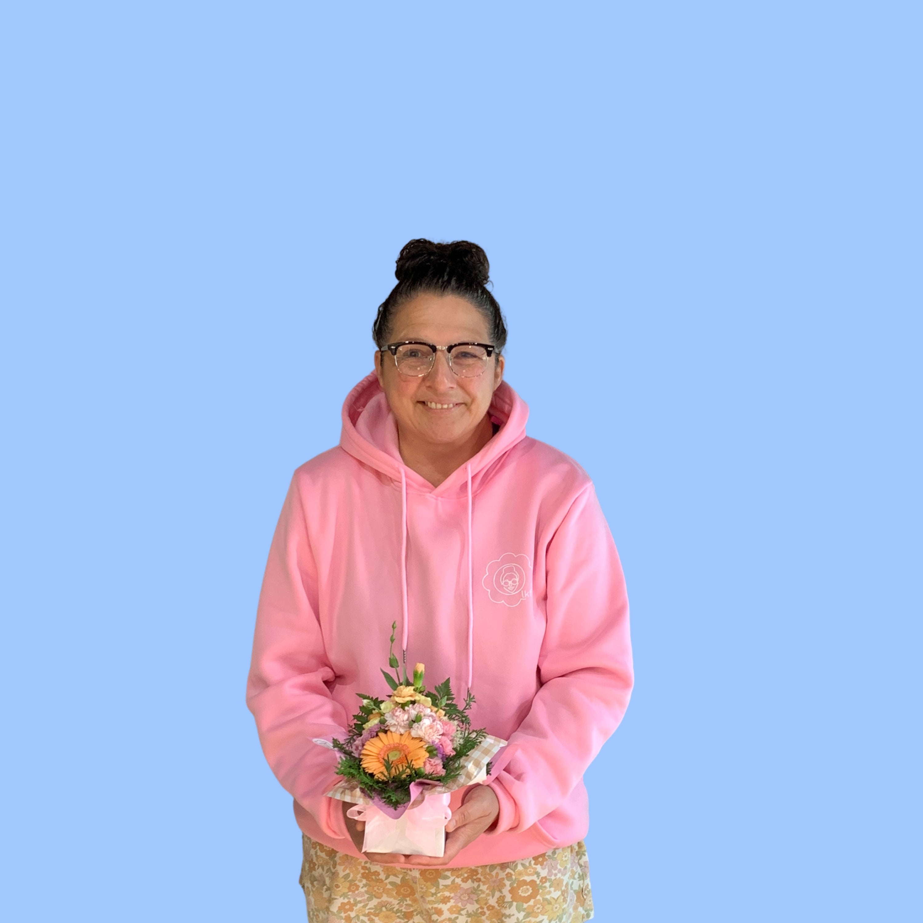 laura king holding Small mixed pastels themed arrangement of flowers wrapped in pink paper displayed in a white posy box with a pink bow around it.