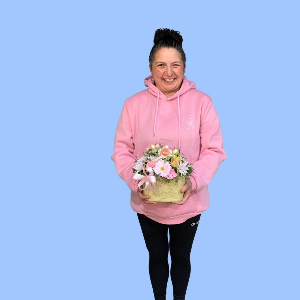 Laura King holds an arrangement of pastels coloured flowers in a small woven style basket with handles and a pink bow