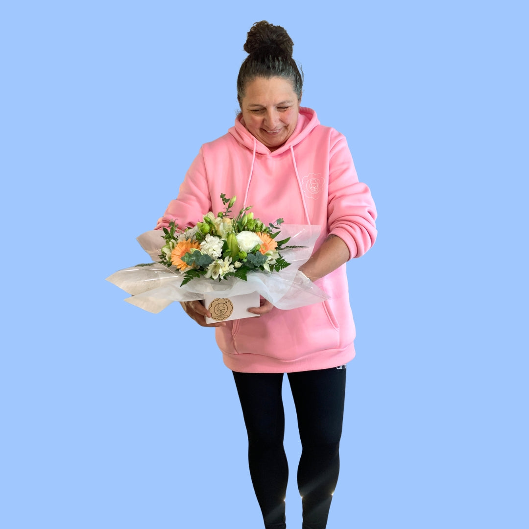 laura king holding an arrangement of apricot and white flowers against greenery and white tissue.