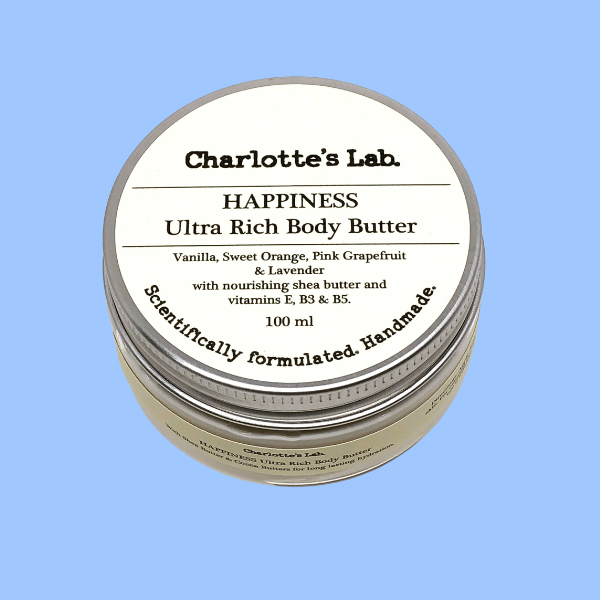 Charlotte's Lab Happiness Ultra Rich Body Butter in a round glass jar with silver metal lid with a cream-colored label, set against a solid light blue background.