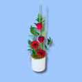 Minimalist arrangement with two staggered red roses placed higher and two lower placed gerberas staggered below. background foliage is tall bamboo and leaf. in a matte white cylindrical ceramic pot.