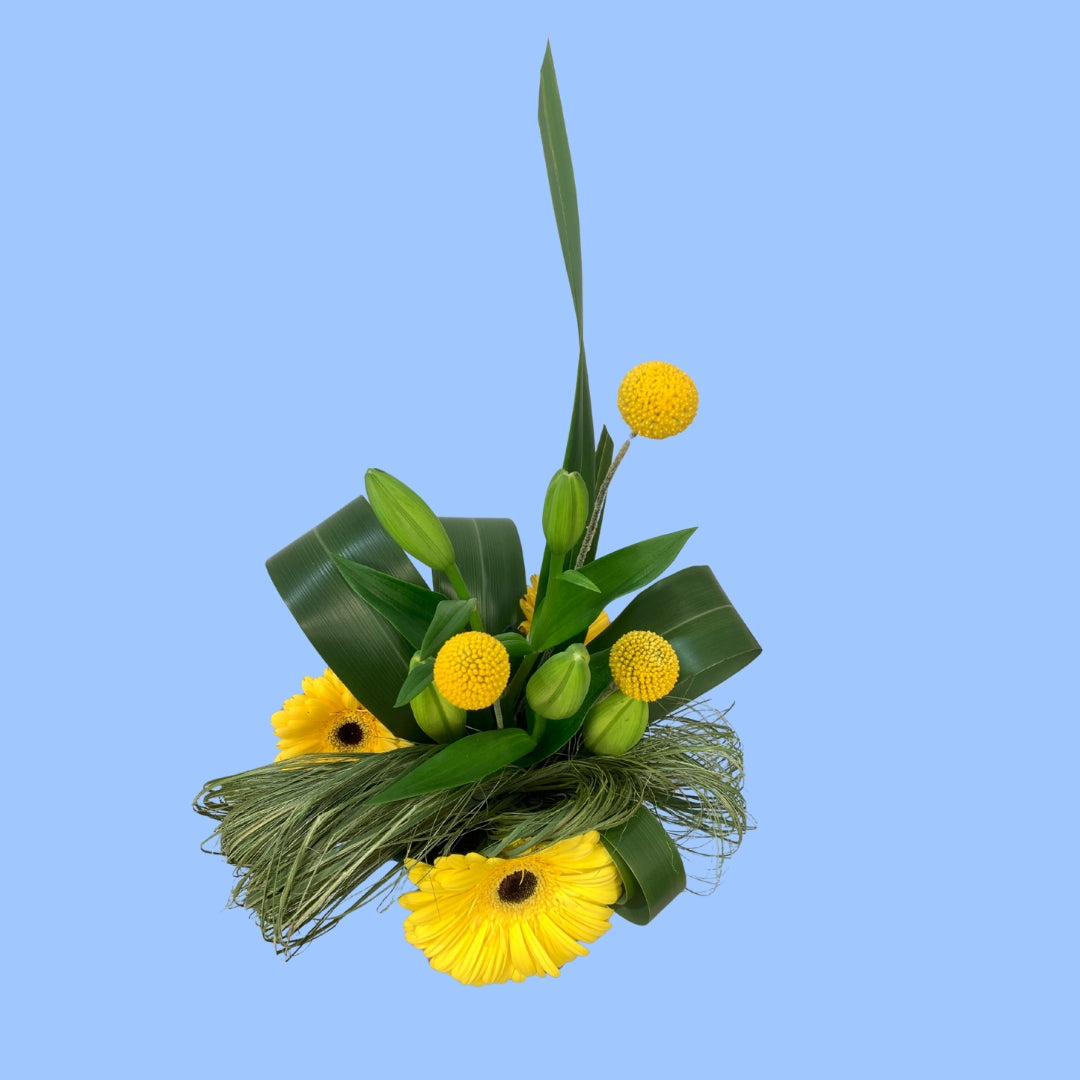 top view of flower arrangement with bright yellow gerberas and yellow ball shaped flowers between artistic flax design and lilies. 