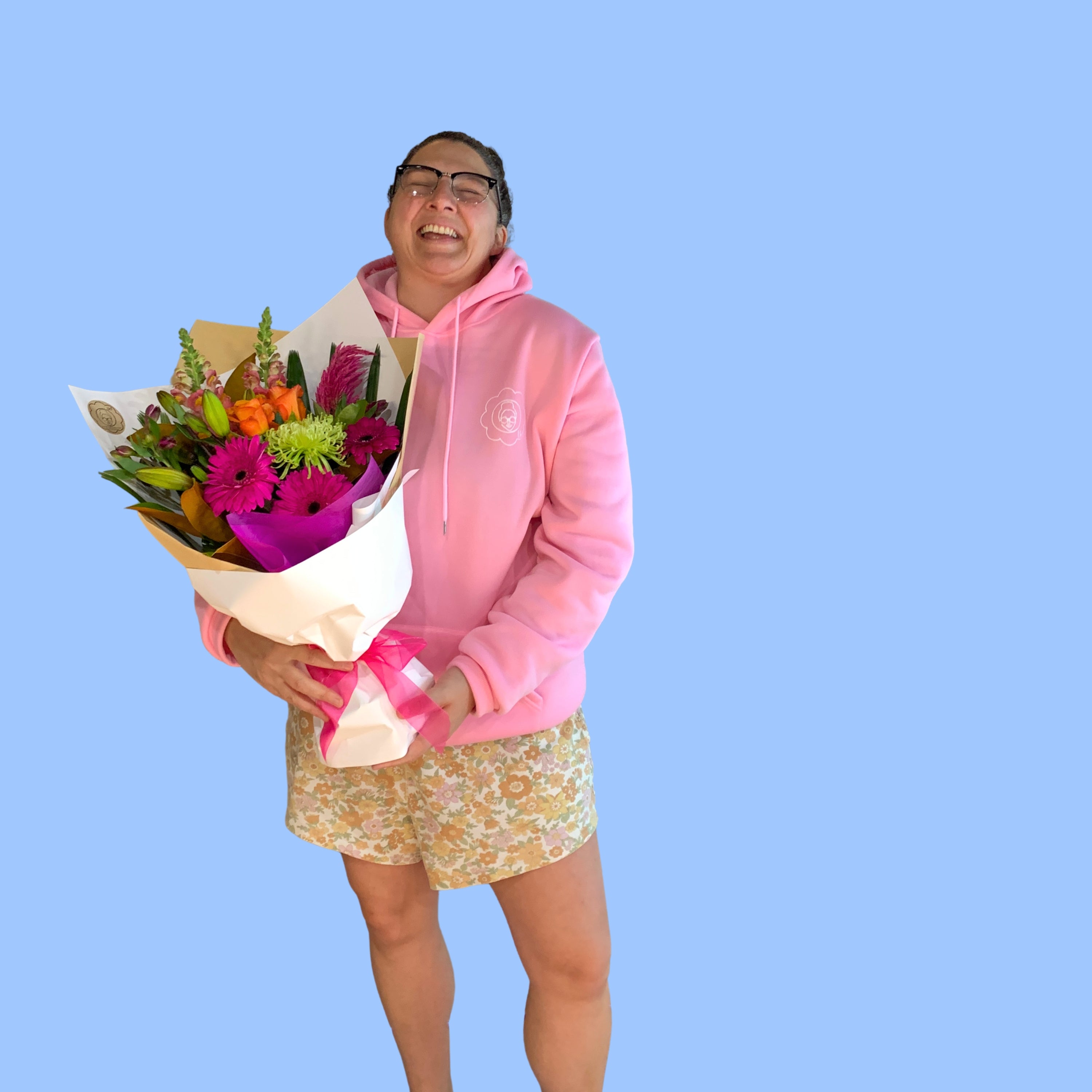 Laura King holding Mixed Bouquet of vibrant coloured flowers wrapped in craft and white with vibrant pink bow.