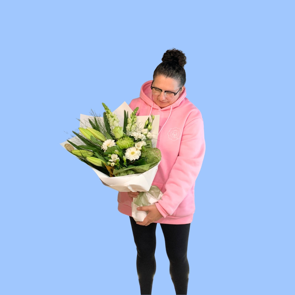 Laura King holding Classic white and green sympathy flower bouquet. wrapped in white with olive green bow