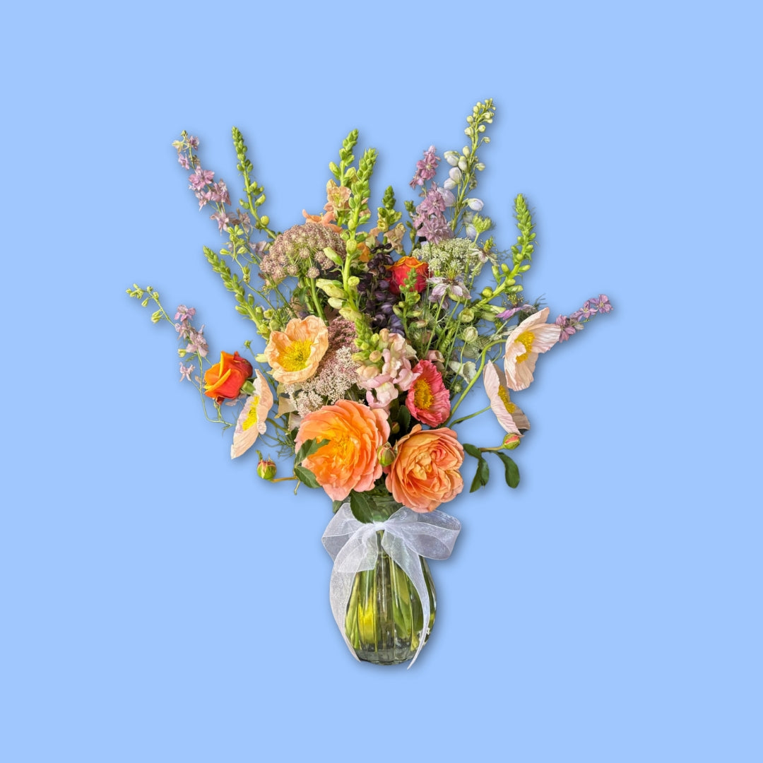 Elegant wild-style flower arrangement in a glass vase with white ribbon bow around it