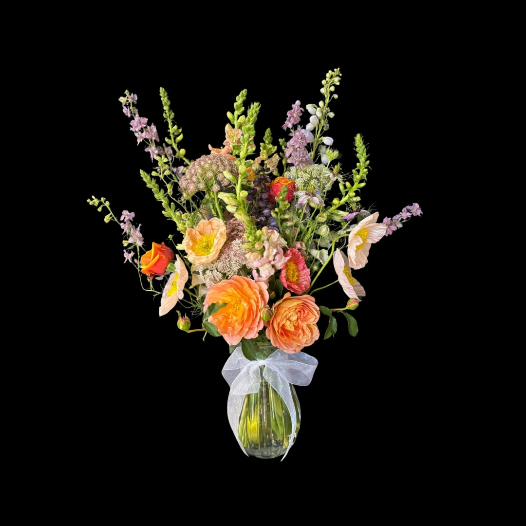 Elegant wild-style flower arrangement in a glass vase with white ribbon bow around it