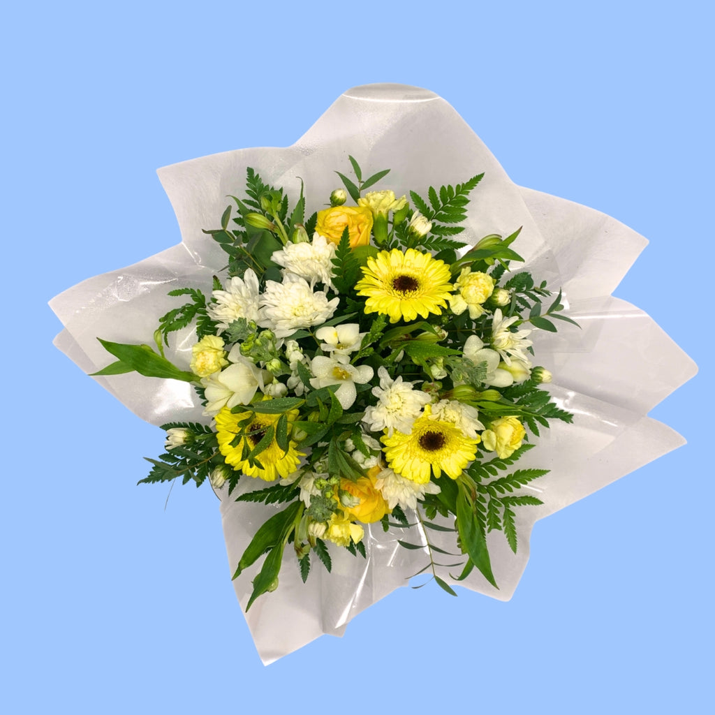 top down view of Bouquet of yellow and white flowers in clear plastic wrap and white tissue 